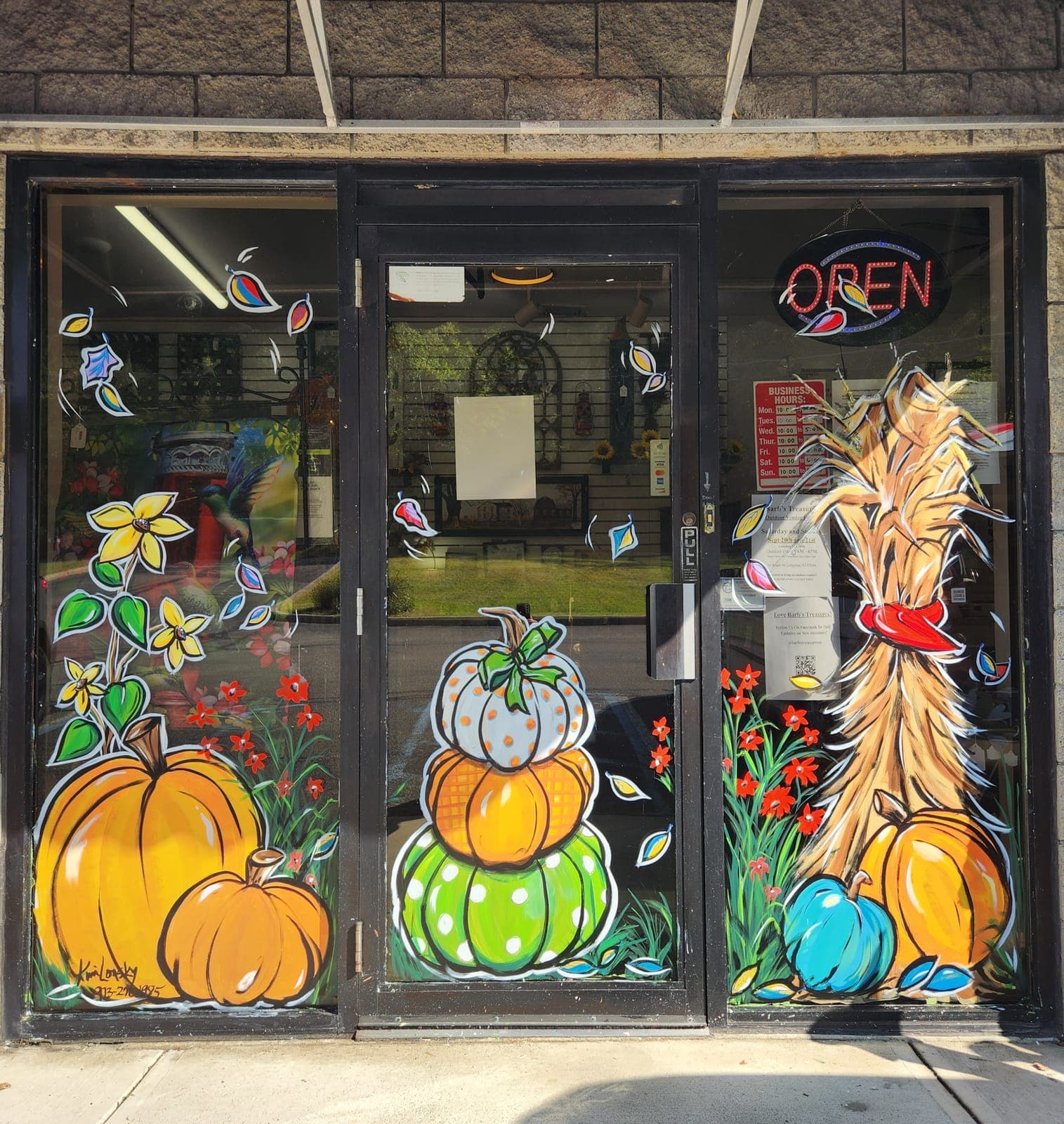 Autumn storefront windows painted with stacked pumpkins, a corn stalk, and falling leaves