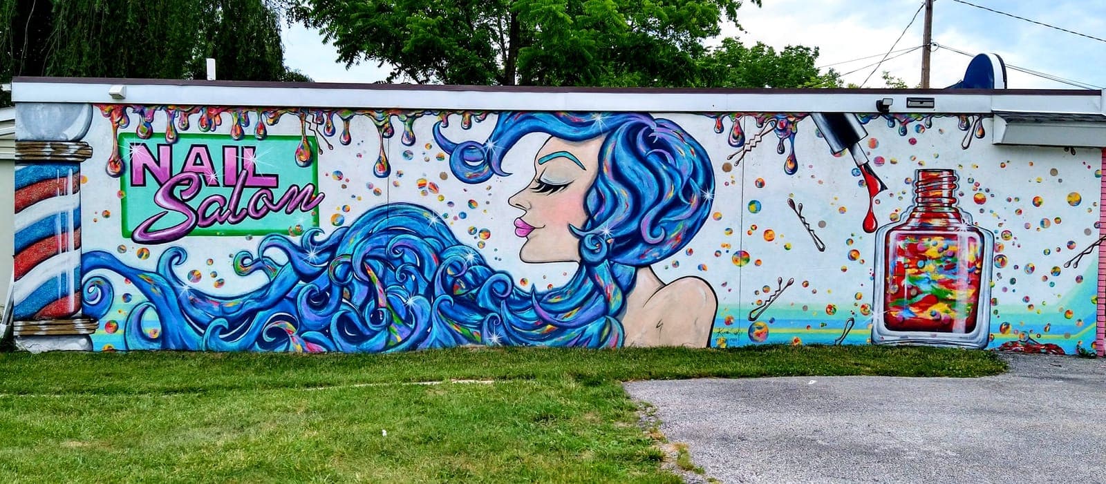 Wall mural of a woman with flowing blue hair beside an oversized nail-polish bottle, painted for a nail salon