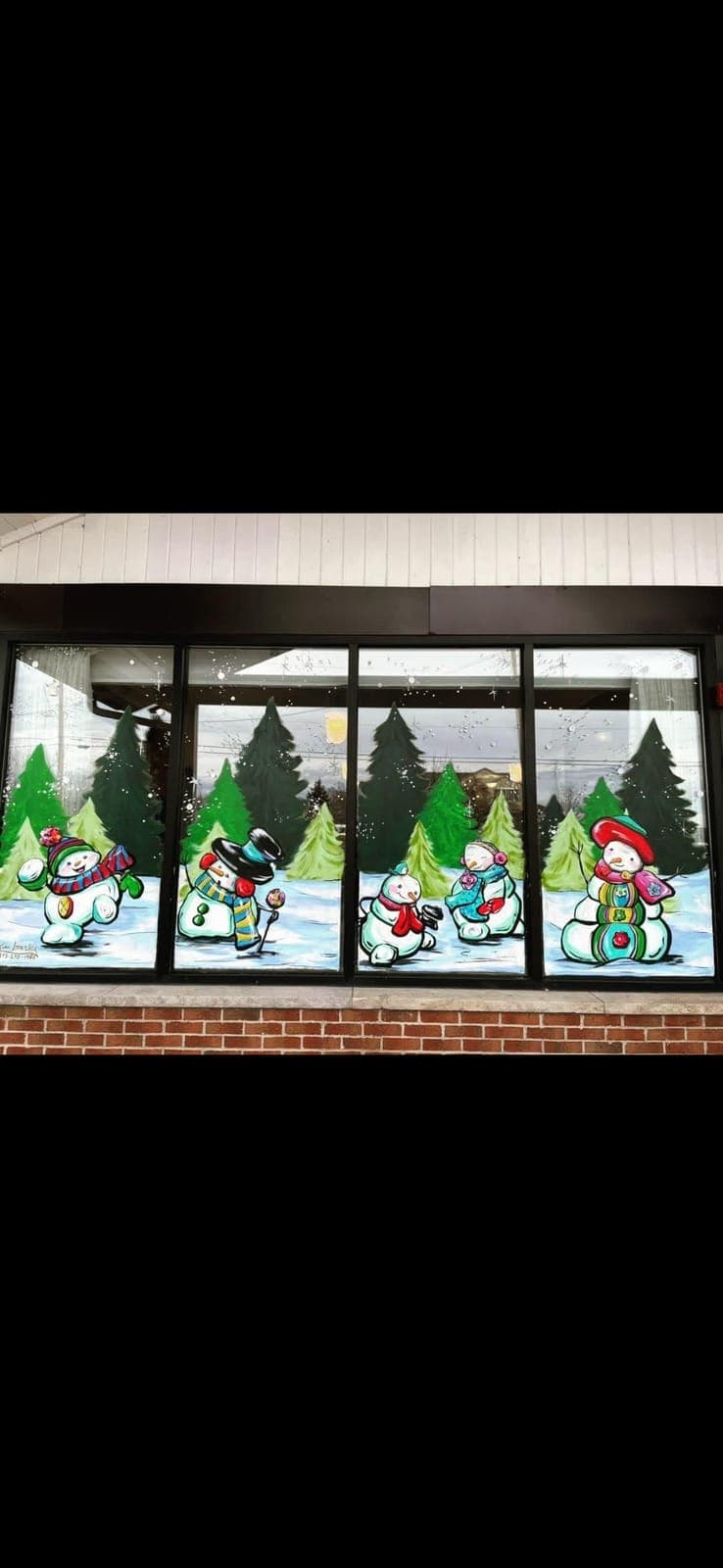 Row of cheerful top-hatted snowmen painted across a brick storefront’s windows